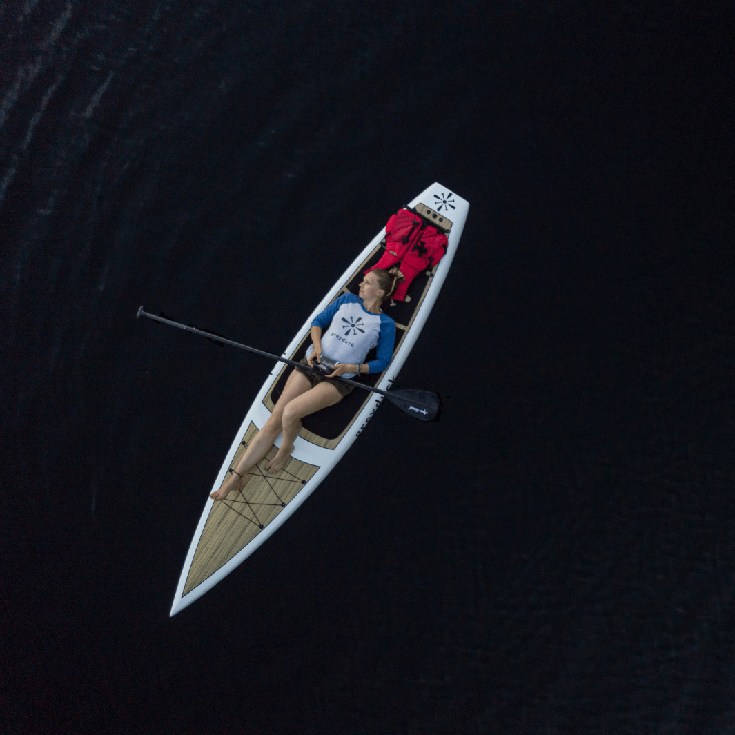 girl laying on Grey Duck paddle board with Malta carbon 2-piece SUP paddle across her body aerial shot