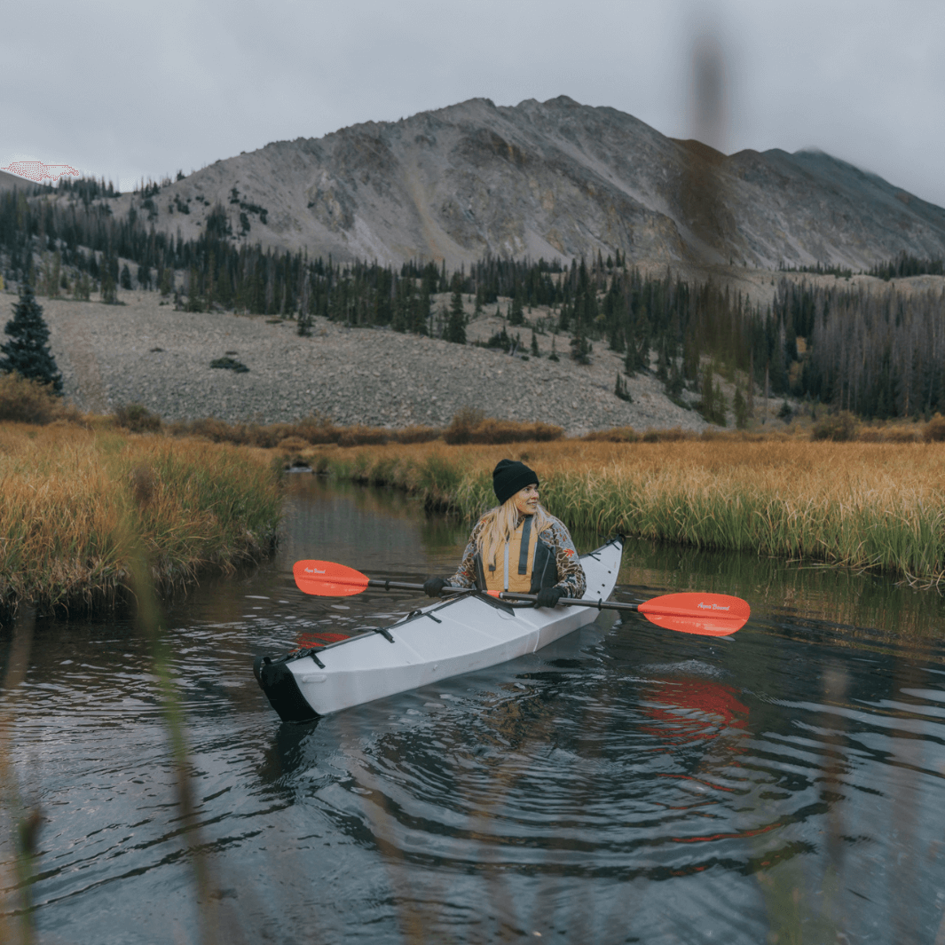 sting ray fiberglass 4-piece snap button sunset red being paddled by blonde woman with rocky mountains in background#color_sunset-red